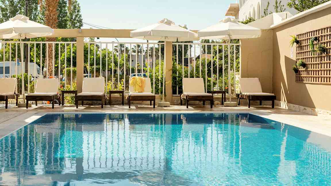 Utendørsbasseng med solsenger og parasoller langs kanten. (AI-generert tekst)