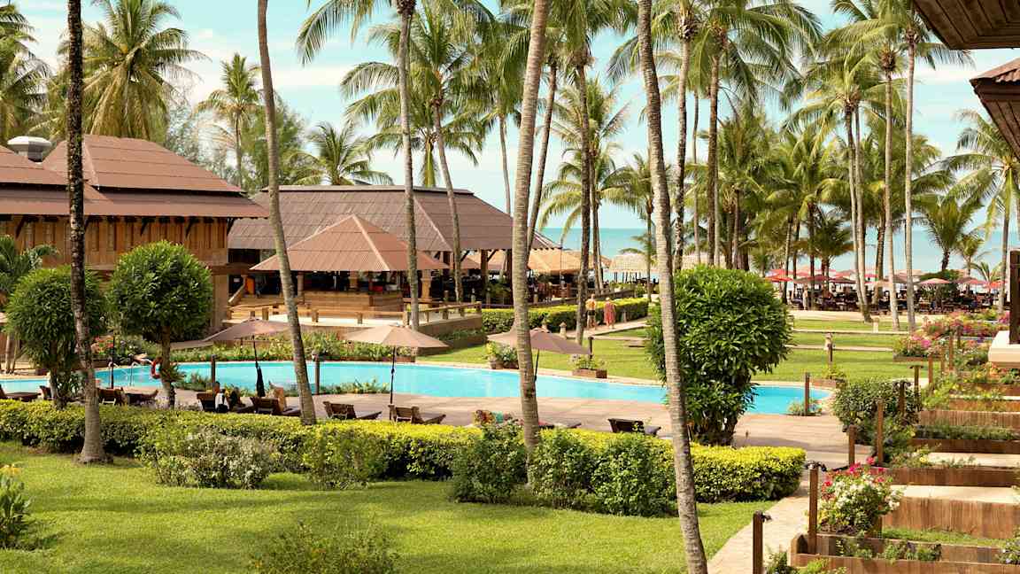 Bilde av en tropisk ferieresort med et basseng omgitt av gressplen, palmer og bygninger. (AI-generert tekst)