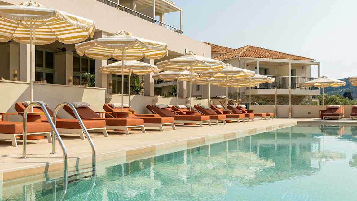 Et basseng omgitt av solsenger og parasoller ved en bygning. (AI-generert tekst)