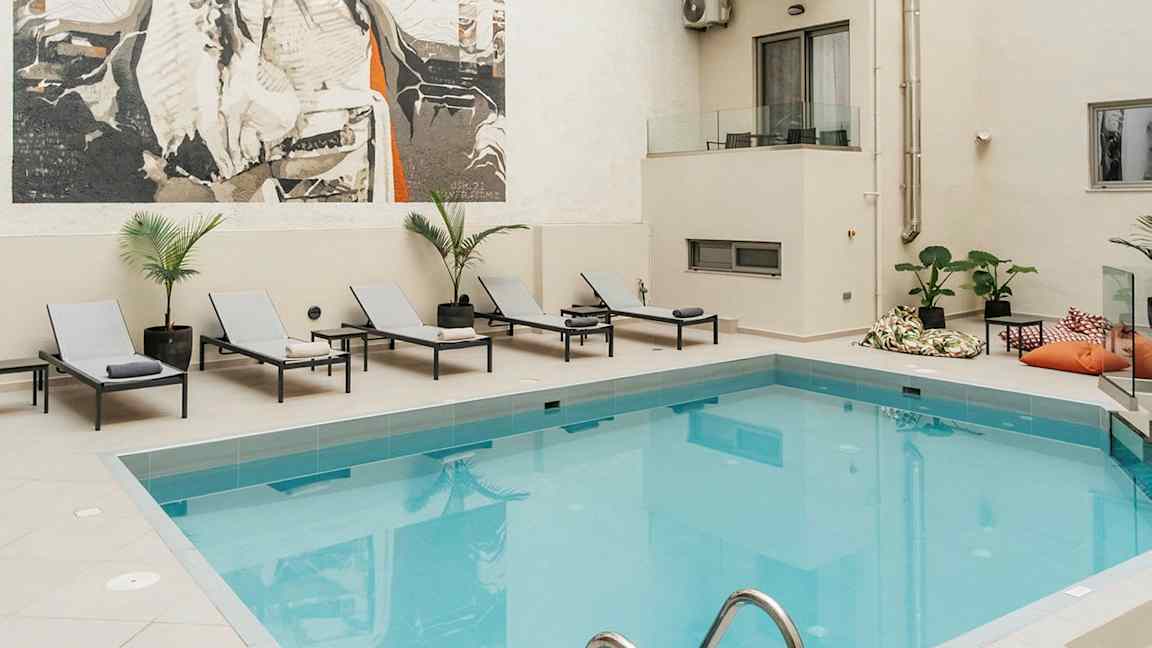 Bilde av et utendørs svømmebasseng ved et hotell med solsenger og et stort kunstverk på veggen. (AI-generert tekst)