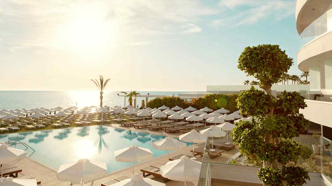 Et utendørsbasseng med solsenger og parasoller, havet i bakgrunnen. (AI-generert tekst)