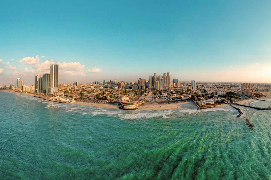 Panoramabilde av en kystby med høye bygninger, strand og hav. (AI-generert tekst)