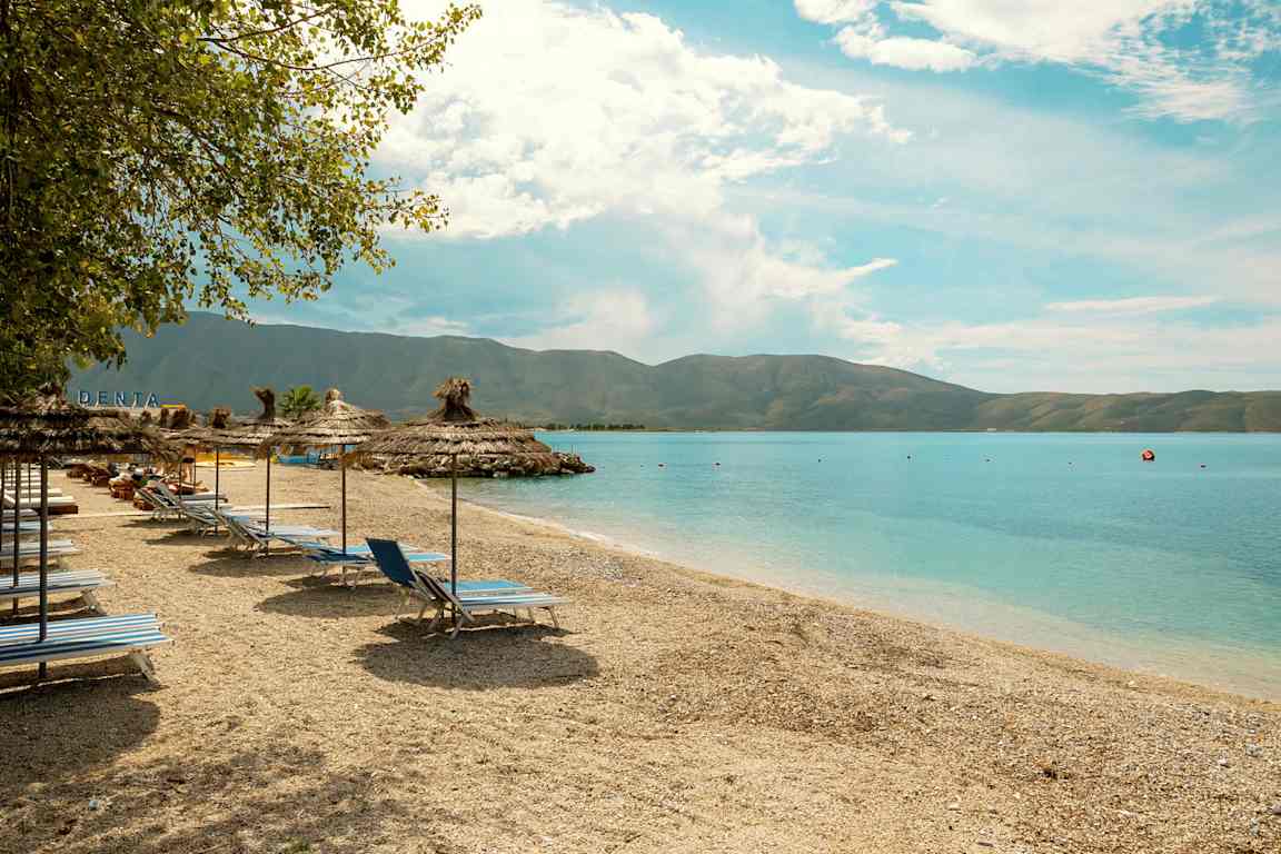 Strand med solsenger og parasoller ved sjøen. (AI-generert tekst)