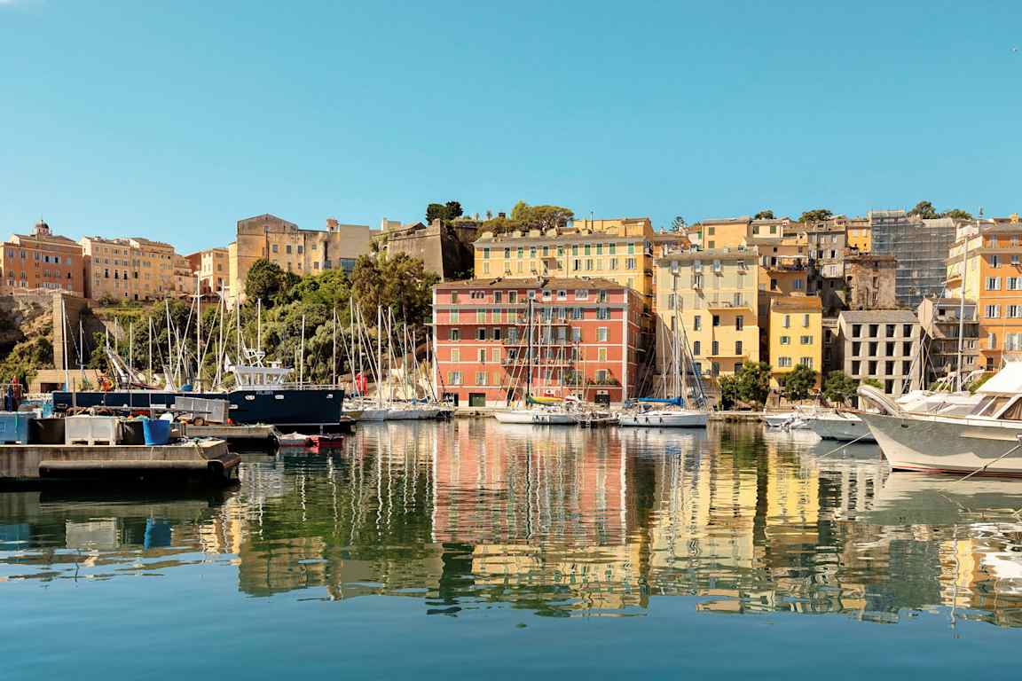 En havn med bygninger i ulike farger og båter ved kaien. (AI-generert tekst)