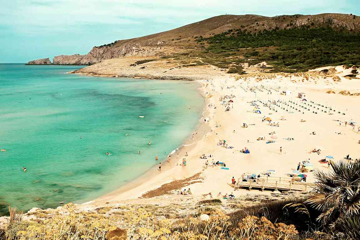 En strand med klart sjøvann, sand og mennesker som soler seg og svømmer. (AI-generert tekst)