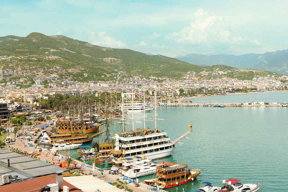 Havn med båter og kystlinjen til byen Alanya i bakgrunnen. (AI-generert tekst)