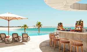 Et basseng ved stranden med solsenger, parasoll og en bassengbar med eksotiske frukter. (AI-generert tekst)