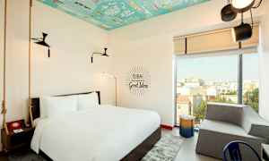 Et hotellrom med en stor seng, moderne interiør og et fargerikt tak. Et stort vindu gir utsikt over byen. (AI-generert tekst)