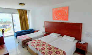 Et hotellrom med to enkeltsenger, en dagseng og et bord ved vinduet. (AI-generert tekst)