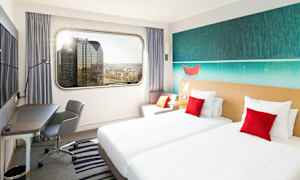 Et hotellrom med to enkeltsenger, en arbeidsplass og en stor vindusutsikt over byens skyline. (AI-generert tekst)