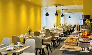 Et moderne restaurantområde med gule vegger, oppsatte bord og en buffé med ulike matvarer. (AI-generert tekst)