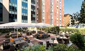 Bilde av en utendørs serveringsområde med bord, stoler og parasoller ved en bygning. (AI-generert tekst)