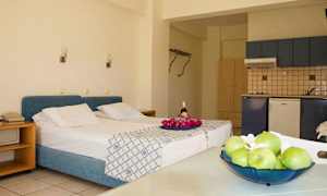 Rommet har en seng med blå sengegavl, et kjøkken og et bord med frukt. (AI-generert tekst)