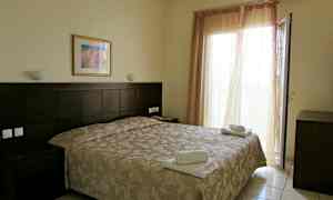 Et hotellrom med en dobbeltseng, nattbord og en åpen balkongdør. (AI-generert tekst)