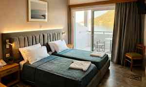 Hotellrom med to enkeltsenger, nattbord og bilde på veggen. Balkong med utsikt over vann og fjell. (AI-generert tekst)
