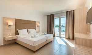 Et lyst hotellrom med to senger, en balkongdør med utsikt og tremøbler. (AI-generert tekst)