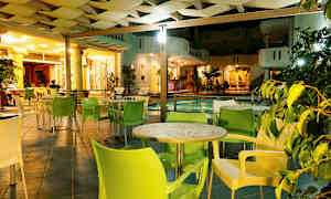 En utendørs lounge med bord og stoler ved siden av et basseng, opplyst om kvelden. (AI-generert tekst)