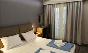 Et hotellrom med en dobbeltseng, skrivebord og et vindu med gardiner. (AI-generert tekst)