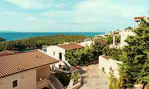 Utsikt over ferieboliger med terrakottatak omgitt av grøntområder, og havet i bakgrunnen. (AI-generert tekst)