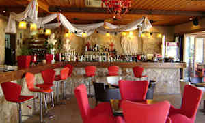 Interiør av en bar med røde stoler og en vegg av stein. (AI-generert tekst)