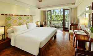 Et hotellrom med en stor dobbeltseng, tregulv og en balkong med utsikt mot grøntområder. (AI-generert tekst)