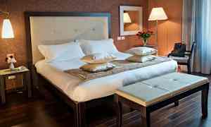 Et hotellrom med en dobbeltseng, sidebord og benk. (AI-generert tekst)