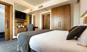 Et hotellrom med en stor seng, en skrivebordsplass med stol og veggmontert TV, samt garderober i tre. (AI-generert tekst)