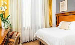 Et hotellrom med en seng, et skrivebord og en stol. Gardiner henger ved et vindu. (AI-generert tekst)