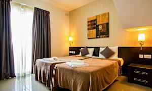 Et hotellrom med to enkeltsenger, nattbord, vegglamper, et maleri over sengene og gardiner ved et vindu. (AI-generert tekst)