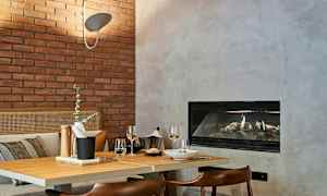 En koselig spiseplass med et bord i tre, en serveringsbrett med tilbehør, to vinglass og peis i bakgrunnen. (AI-generert tekst)