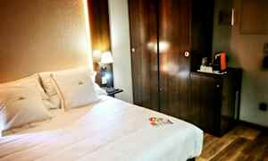 Et hotellrom med en seng og opplyst nattlampe ved siden av et mørkt treskap. (AI-generert tekst)