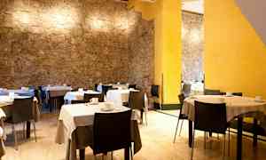 Et rom med bord og stoler, hvit duk og kaffekopper samt steinvegger og gule veggdetaljer. (AI-generert tekst)