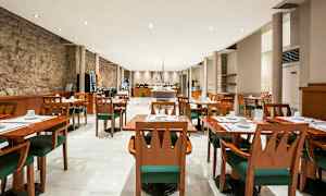 Et romslig restaurantområde med tremøbler, hvite duker, grønne stoler og en moderne innredning. (AI-generert tekst)