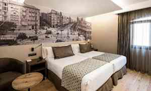 Et hotellrom med en dobbeltseng, to puter, moderne innredning og et fototapet som forestiller et bymiljø på veggen. (AI-generert tekst)