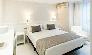 Et lyst og moderne hotellrom med en bred seng, to nattbord og lenestol ved vinduet. (AI-generert tekst)