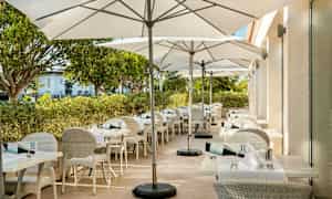 En utendørsterrasse med hvite bord og stoler samt hvite parasoller. (AI-generert tekst)