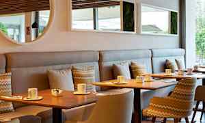 En moderne kafé med trebord, stoler og sofaer. På bordene står kopper og små skåler. (AI-generert tekst)