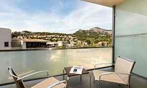 Balkong med to stoler, et bord og en glasskjerm med utsikt over et fjellområde og en urban setting. (AI-generert tekst)