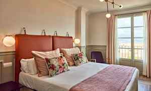 Et hotellrom med en seng, dekorative puter og et vindu som viser utsikt. (AI-generert tekst)