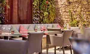 En uteplass med sitteplasser og dekorerte vegger, omgitt av grøntområder. (AI-generert tekst)