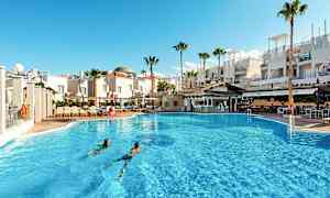 Et stort utendørs basseng foran hvite bygninger og palmer. (AI-generert tekst)