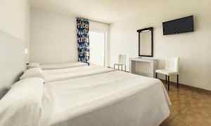 Et hotellrom med tre enkeltsenger, et skrivebord med speil, to stoler og en veggmontert TV. (AI-generert tekst)