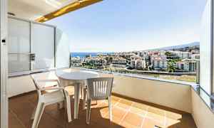 En balkong med bord og stoler som vender ut mot en utsikt over byen og sjøen. (AI-generert tekst)