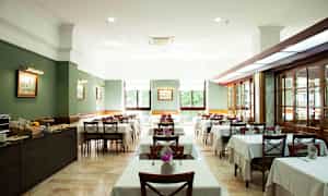 Interiør av en restaurant med dekkede bord og stoler. (AI-generert tekst)