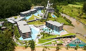 Luftfotografi av et hotellområde med bassenger og omkringliggende grøntområder. (AI-generert tekst)