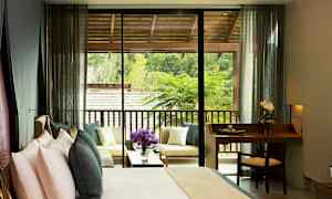 Et hotellrom med en seng og en liten skrivebordsplass, samt en terrasse med sittemøbler og utsikt over grøntområder. (AI-generert tekst)