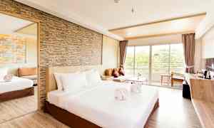 Et romslig hotellrom med en stor seng, sandsteinsvegg, speil, sofa og vindu som fører til en balkong. (AI-generert tekst)