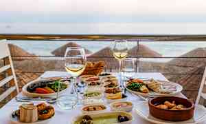 Et dekket bord med forskjellige retter og vinglass, med utsikt over stranden og havet. (AI-generert tekst)