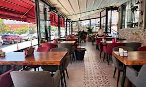 Bilde av en restaurant med rødt interiør, trebord og polstrede stoler. Utsikt over gaten sees gjennom glassvinduer. (AI-generert tekst)