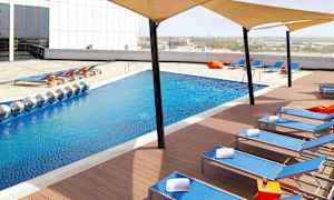 Et moderne basseng med blått vann omgitt av solsenger og skyggetak. (AI-generert tekst)